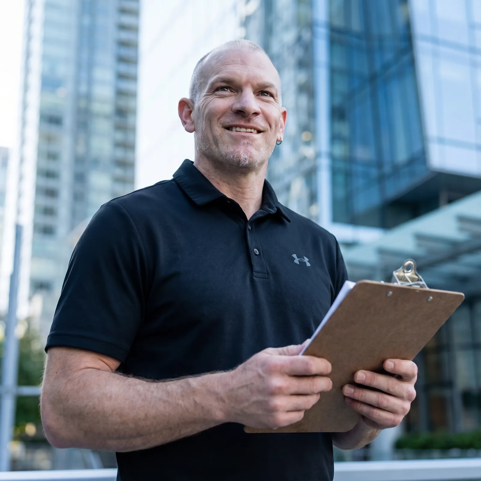 Brody Robertson smiling outdoors in front of glass buildings, holding a clipboard of scope sheets